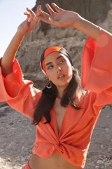 Blusa naranja con mangas largas acampanadas y nudo en la parte delantera.