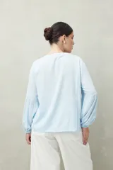 Camisa celeste de corte holgado con botones frontales, canesú con tablas y mangas 3/4 amplias con puño elastizado.