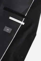 Blazer negro de corte ajustado, con solapas de muesca finas, botonadura sencilla con dos botones, bolsillo superior, bolsillos delanteros con solapa, tres bolsillos interiores, botones decorativos en los puños y abertura atrás. Forrado.