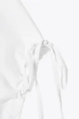 Camiseta blanca de algodón con cuello redondo, corte recto y mangas cortas ajustables con lazadas.