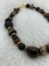 Collar corto con cuentas de piedra volcánica negra, cuentas de madera en tonos marrones y beige, y detalles metálicos dorados.