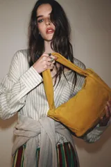 Bolso de mano color mostaza, de serraje, con asa ancha con detalles y cierre mediante hebilla metálica.
