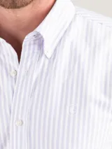 Camisa de hombre Oxford a rayas celestes y blancas, confeccionada en 93% algodón y 7% algodón reciclado. Corte regular fit, cuello button-down, cierre con botones, manga larga con puño simple y logo bordado en el pecho.