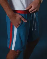 Short de jogging celeste con cintura elástica y cordón blanco. Tiene una franja vertical blanca y roja en los laterales.