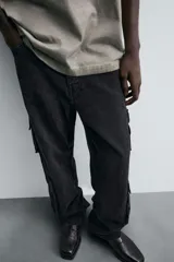 Pantalón de denim color beige, corte relaxed fit, con bolsillos laterales tipo cargo con solapa y cierre de botón. Cierre frontal con botón y cremallera.