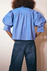 Camisa de cuello redondo con estampado de rayas verticales azules y blancas, manga larga abullonada y cierre frontal con botones.