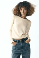 Sweater negro de punto liso con cuello redondo y mangas largas con botones dorados en los puños.
