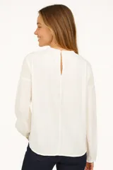 Blusa color marfil con detalles de encaje en el frente y los hombros, de mangas largas y corte holgado.