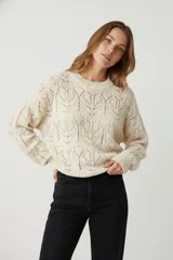 Sweater de punto color crudo, con cuello redondo y tejido calado con diseño de hojas o espigas.