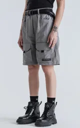 Bermuda cargo color gris oscuro (carbón), de corte recto y largo hasta la rodilla, con cinturón de cinta negra ajustable con hebilla de plástico. Presenta bolsillos laterales y bolsillos cargo con solapa en las piernas.