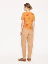 Remera color mostaza de punto flamé con estampado de labios rojos, escote en V profundo, mangas cortas y corte a la altura de la primera cadera.