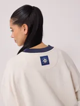 Sweater color ladrillo con cuello redondo en color crema. Estampado frontal con el texto 'Malibu Rusty' y un logo con forma de flor. Corte holgado.