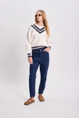 Buzo de punto color crudo con escote en V y rayas azul marino en cuello, puños y ruedo.