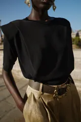 Top negro de tejido de punto, cuello redondo, manga corta y hombreras marcadas. Presenta un bajo ancho y ajustado.