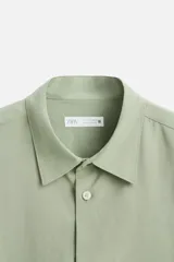 Camisa verde claro de corte relaxed fit confeccionada en tejido con mezcla de modal. Tiene cuello italiano, manga larga con puños abotonados, bolsillo de parche en el pecho y cierre frontal abotonado.