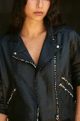 Chaqueta de cuero ovino color negro, estilo biker, con cuello con solapas, cierre metálico descentrado, mangas balloon con puños ajustados y cinturón con hebilla en la cintura.