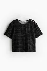 Top de bouclé negro con diseño a cuadros, cuello redondo y mangas cortas. Presenta botones decorativos en el hombro.