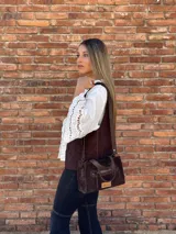 Cartera bandolera de cuero color marrón chocolate, con forro de tela y herrajes dorados. Tiene doble asa de mano y correa larga regulable y desmontable. Incluye bolsillo frontal con cierre y bolsillo interno.