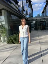 Chaleco blanco de cuero sintético con cierre cruzado, cuello solapa y cinturón con hebilla.