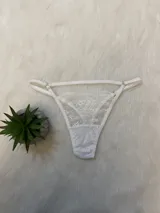 Conjunto de lencería blanco de encaje elastizado, compuesto por un corpiño triangular con breteles regulables, una tanga regulable con portaligas y ligas incluidas.