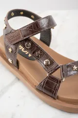 Sandalias marrones de cuero con suela gruesa y tachas doradas en forma de estrella y circulares.