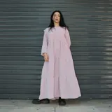 Vestido maxi lila de silueta suelta con volados en los hombros y falda escalonada. Tiene mangas largas y escote redondo.