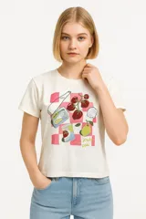 Remera de algodón color crudo con estampado de alimentos sobre fondo a cuadros rosados, corte al cuerpo, cuello redondo y mangas cortas.