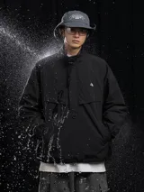 Chaqueta tipo anorak impermeable de color negro, con cuello alto y cierre parcial frontal. Presenta un pequeño logo en el pecho y ajuste regulable en la cintura para un calce más holgado o ceñido.