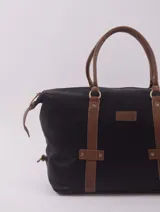 Bolso de viaje negro con detalles en cuero marrón, doble asa de mano y cierre superior con cremallera.