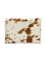 Porta documentos con diseño de piel de vaca en tonos blanco y marrón, confeccionado en cuero con textura de pelo y costuras perimetrales visibles.