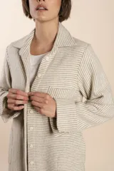 Camisa larga color crema con rayas verticales finas en gris, con botones dorados y bolsillo plaque en la delantera.