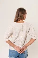 Blusa color crema con bordado de hojas, escote redondo, mangas 3/4 abullonadas con elástico en los puños y cierre con botones en la espalda.