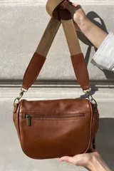 Bandolera de cuero celeste con correa de cinta regulable, forro de algodón, cierre central y bolsillo trasero con cierre.