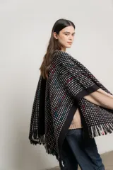 Ruana tejida color negro con diseño geométrico en blanco, celeste y rojo. Presenta cuello abierto y flecos en el ruedo.