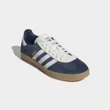 Championes Adidas Gazelle Indoor, color azul marino con tres franjas y detalles en blanco. Presentan un exterior de gamuza y cuero sintético, forro blanco y suela de goma traslúcida color caramelo.