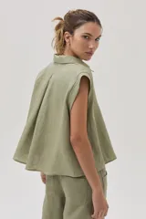 Blusa verde militar sin mangas, confeccionada en lino, con cuello camisero, cierre frontal con botones y corte holgado.