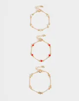 Set de tres pulseras doradas con dijes de flores de metal y resina en color blanco, rojo y dorado.