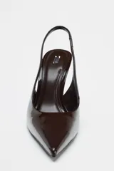 Zapato de tacón tipo cuña destalonado en charol color marrón chocolate. Tacón con forma asimétrica. Tira trasera con pieza elástica. Acabado en punta.