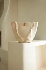 Bolso tipo tote confeccionado en soga de algodón color crudo, con asas de hombro y broche de bronce.