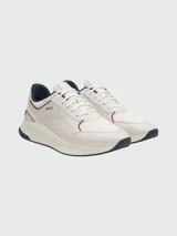 Zapatillas deportivas Boss modelo TTNM EVO, color blanco hueso con detalles en azul marino y ribetes rojos. Presentan una combinación de malla transpirable y paneles de cuero liso con perforaciones. La suela es gruesa y curvada, con detalles en azul marino en la puntera y el talón.