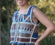 Chaleco corto de denim azul con bordado artesanal en tonos naranja, blanco y marrón. Tiene escote cuadrado, cierre de botones y terminaciones desflecadas.