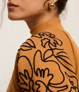 Sweater color ocre con cuello alto y mangas largas con sisas raglán. El sweater tiene bordados de flores en los laterales de las mangas.