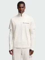 Remera de algodón Moncler Grenoble en color blanco roto con diseño de doble capa. Cuenta con cuello alto, cierre de cremallera corta, logo en el pecho y mangas largas con orificios para el pulgar y detalles tricolores.