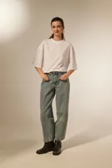 Pantalón jean color blanco, de corte barrel y tiro bajo, con detalles de tachas metálicas en los bolsillos delanteros y a lo largo de las costuras laterales.