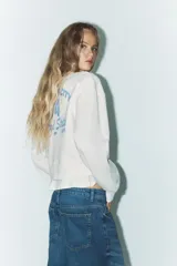 Sudadera corta color crudo de algodón, con cuello redondo, mangas largas y texto estampado en el frente que dice "IN MY YEEHAW ERA".