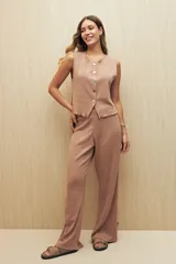 Conjunto de chaleco y pantalón color tostado, de tejido de punto. El chaleco es sin mangas, con cuello redondo y abotonado al frente. El pantalón es de corte palazzo, con elástico en la cintura y aberturas laterales en el ruedo.