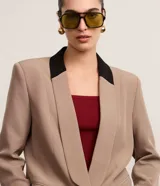Blazer de tejido plano color beige con estructura de sastrería, cuello smoking con contraste negro en la nuca, botón único para cierre y solapas delanteras que simulan bolsillos.