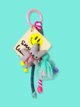 Llavero con dije de tela con carita sonriente, estrella de peluche gris, borla de hilo turquesa y cordones de colores.