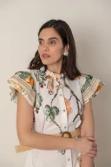 Vestido midi camisero de algodón color natural con estampado de flores, animales y ramas en tonos rojo, marrón, verde y azul. Tiene cuello mao, mangas cortas con volados, bolsillos laterales y cinturón de soga color beige.