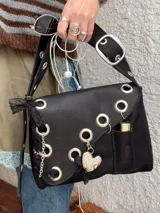 Cartera de cuero negra con correa regulable, estilo bandolera o al hombro. Decorada con charm de corazón metálico, encaje negro, cadenas y aros metálicos.